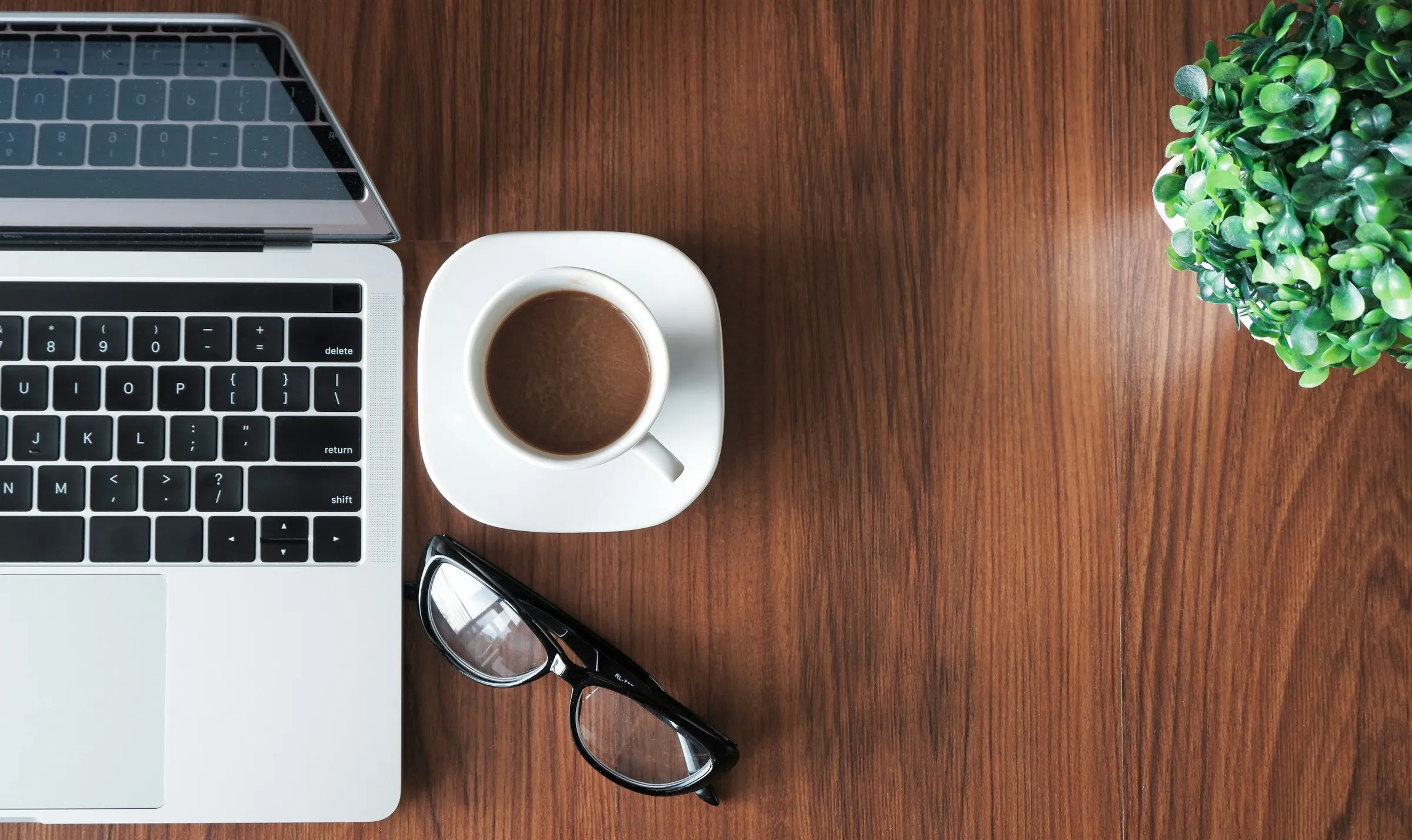 Kaffekopp, briller og laptop på et skrivebord